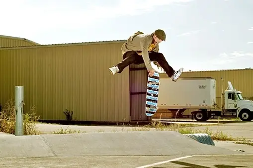 Skater leaping over his skateboard beside a warehouse in Colorado