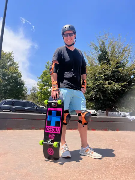 Adult beginner skateboarder in helmet, knee and wrist pads at a Denver-area skatepark