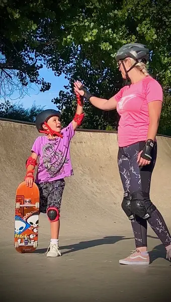 Young girl high-fiving her mom in a skatepark bowl during a family skateboard lesson