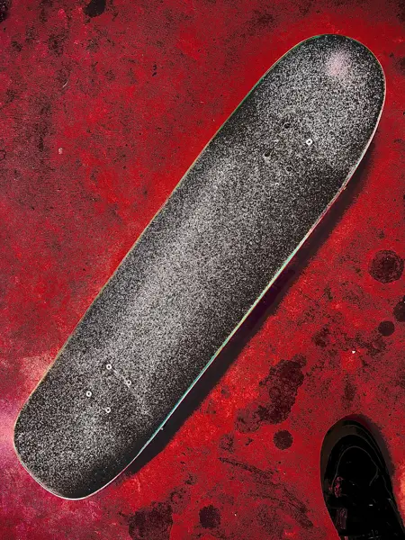 Close-up of a skateboard deck with fresh grip tape on a red surface