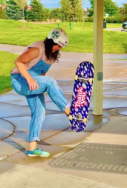 Woman in overalls learning to flip her skateboard up at a Colorado park